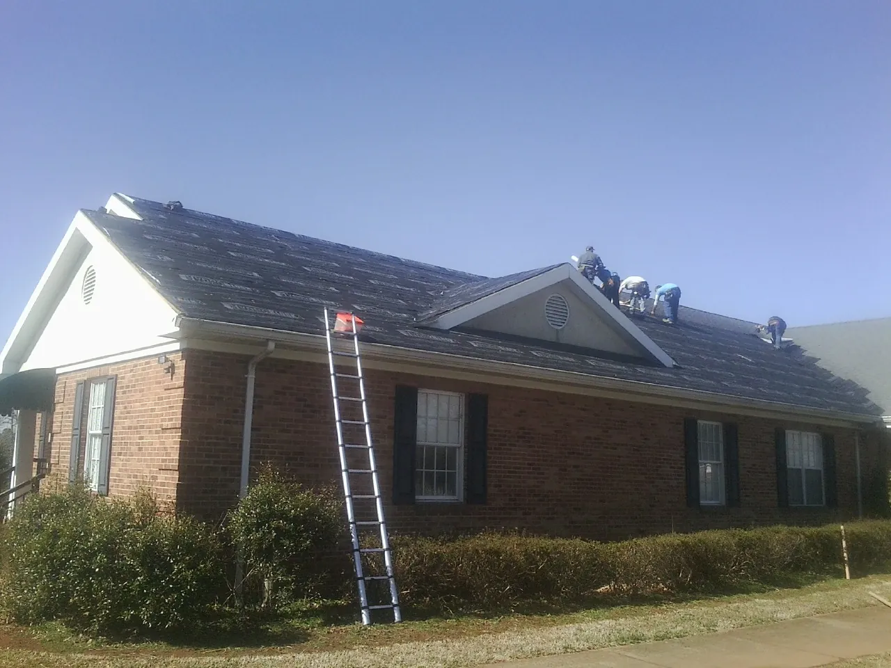 Crew tearing shingles off a brick ranch roof with a ladder set — Emergency Roof Repair work by our crew in Camak