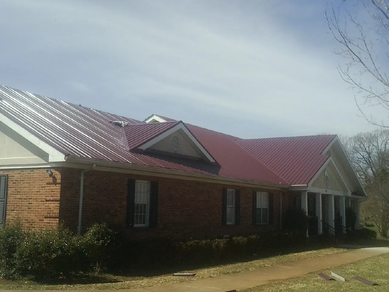 Red metal roof with gabled entries on a long brick building, from a Hail Damage Roof Repair job in Camak