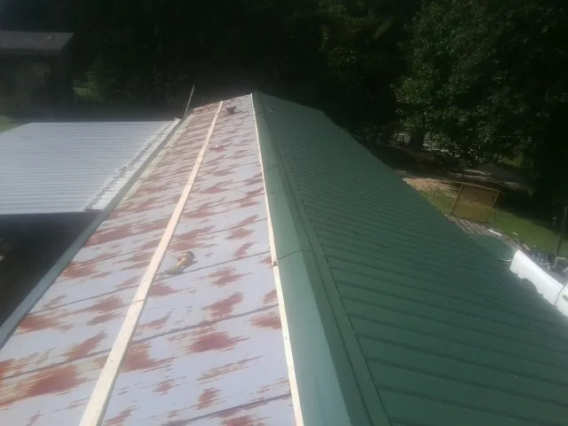 Old rusted panels beside newly installed green metal roofing — Wind Damage Roof Repair by Roofing Brothers in Camak