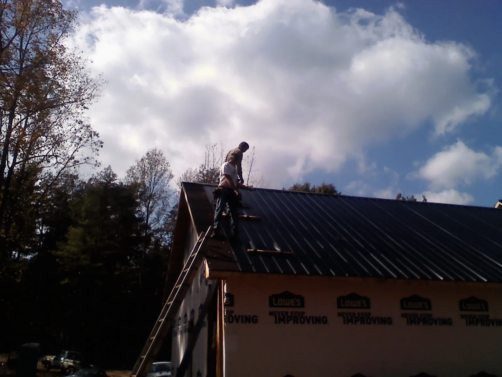 Roofer fastening dark metal panels high against a cloudy sky, from a Roof Inspection job in Camak