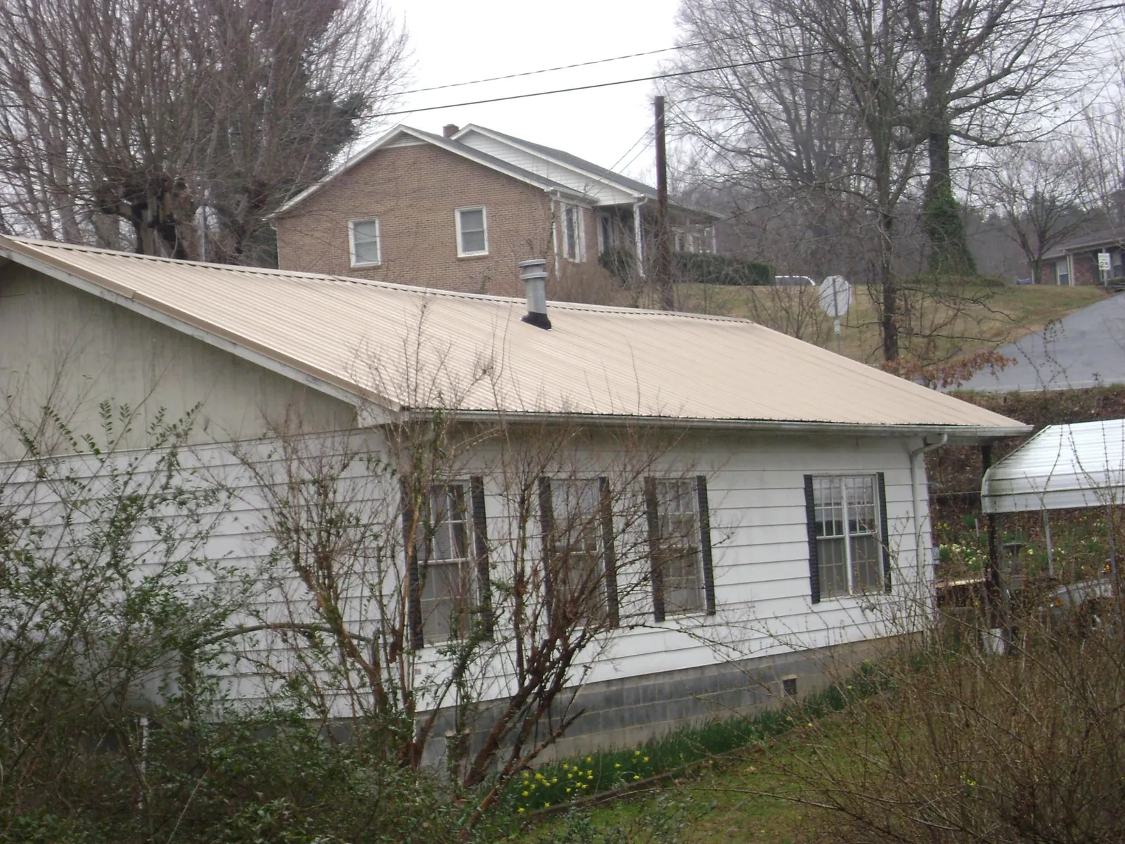 Tan metal roof on a white sided house set into a hillside — Commercial Roofing by Roofing Brothers in Camak